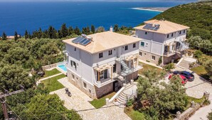 Uma casa de dois andares com painéis solares, piscina e vista para o mar.