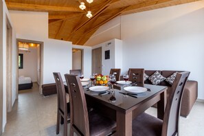 A dining area with a wooden ceiling, a glass table, and brown chairs.
