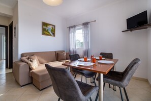 A modern living room with a sofa, dining table, chairs, a flat-screen TV, and a painting on the wall. - Holiday Apartment with Sea View 'Α' with Pool, Garden, Terrace & Wi-Fi (?e???da)
