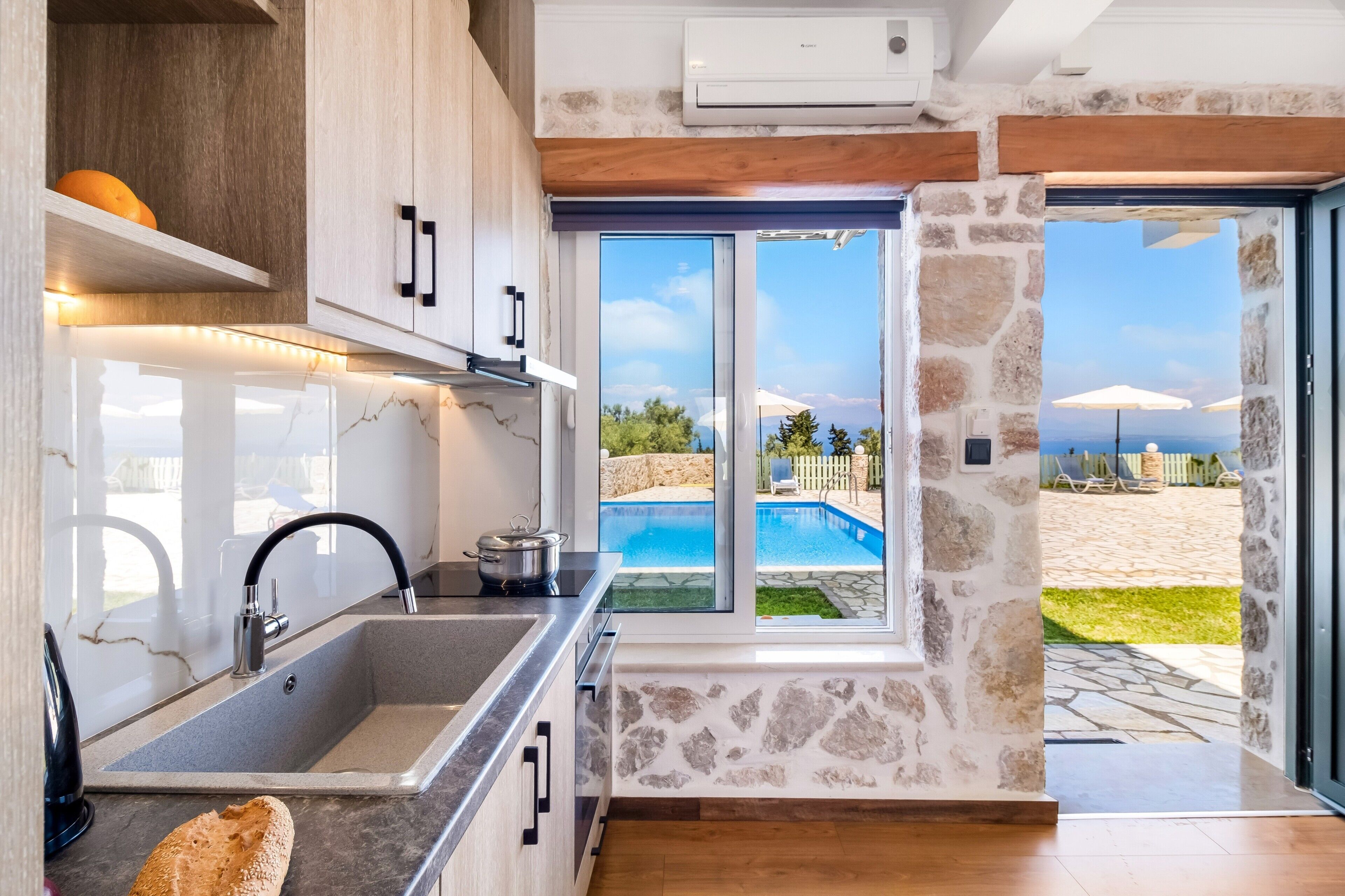 A modern kitchen with a large window, stone wall, and a view of a pool and beach.