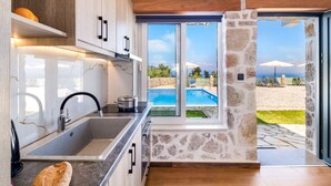 A modern kitchen with a large window, stone wall, and a view of a pool and beach. - Apartment with Pool View, Sea View, Wi-Fi & Terrace (?e???da)