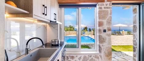 A modern kitchen with a large window, stone wall, and a view of a pool and beach.