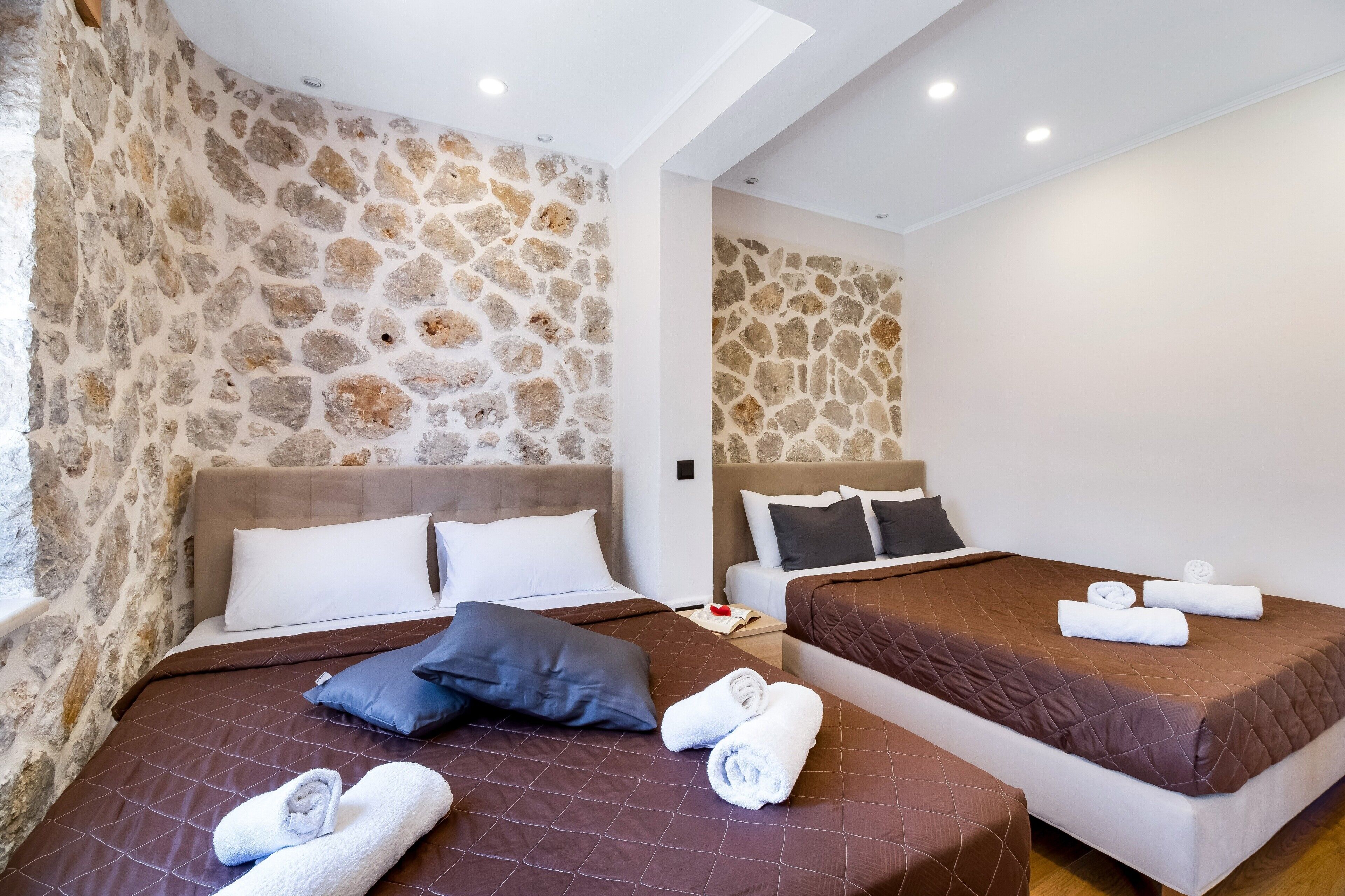 A room with two beds, stone walls, and a skylight.