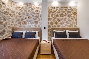 A room with two beds, stone walls, and a wooden nightstand with a book.