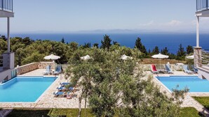 A pool area with two pools, lounge chairs, umbrellas, and a view of the sea. - 'Apartment with Sea View B' with Pool, Garden, Terrace & Wi-Fi (?e???da)