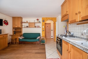 Une cuisine compacte avec des meubles en bois, un canapé vert et un petit coin repas.