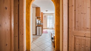 A hallway with wooden doors and an archway leading to a kitchen area with a refrigerator, sink, and window. - Holiday Apartment 'Le Coccinelle' with Mountain View, Terrace & Wi-Fi (Varena)