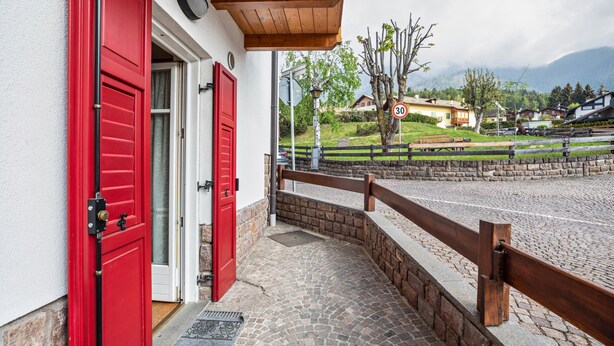 A building with red doors, a cobblestone pathway, and a view of a mountain. - Holiday Apartment 'Le Coccinelle' with Mountain View, Terrace & Wi-Fi (Varena)