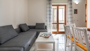 A living room with a grey sofa, a white coffee table, and a dining area with white chairs and a table.