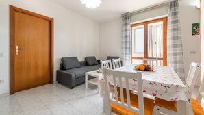 A living room with a sofa, dining table, chairs, and a window with curtains.
