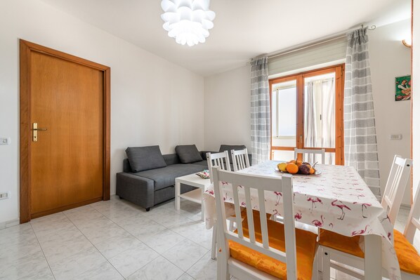 Un salon comprenant un canapé, une table à manger, des chaises et une fenêtre avec des rideaux.