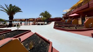 Ett semesterhotell med en pool, palmer och en röd och gul byggnad.