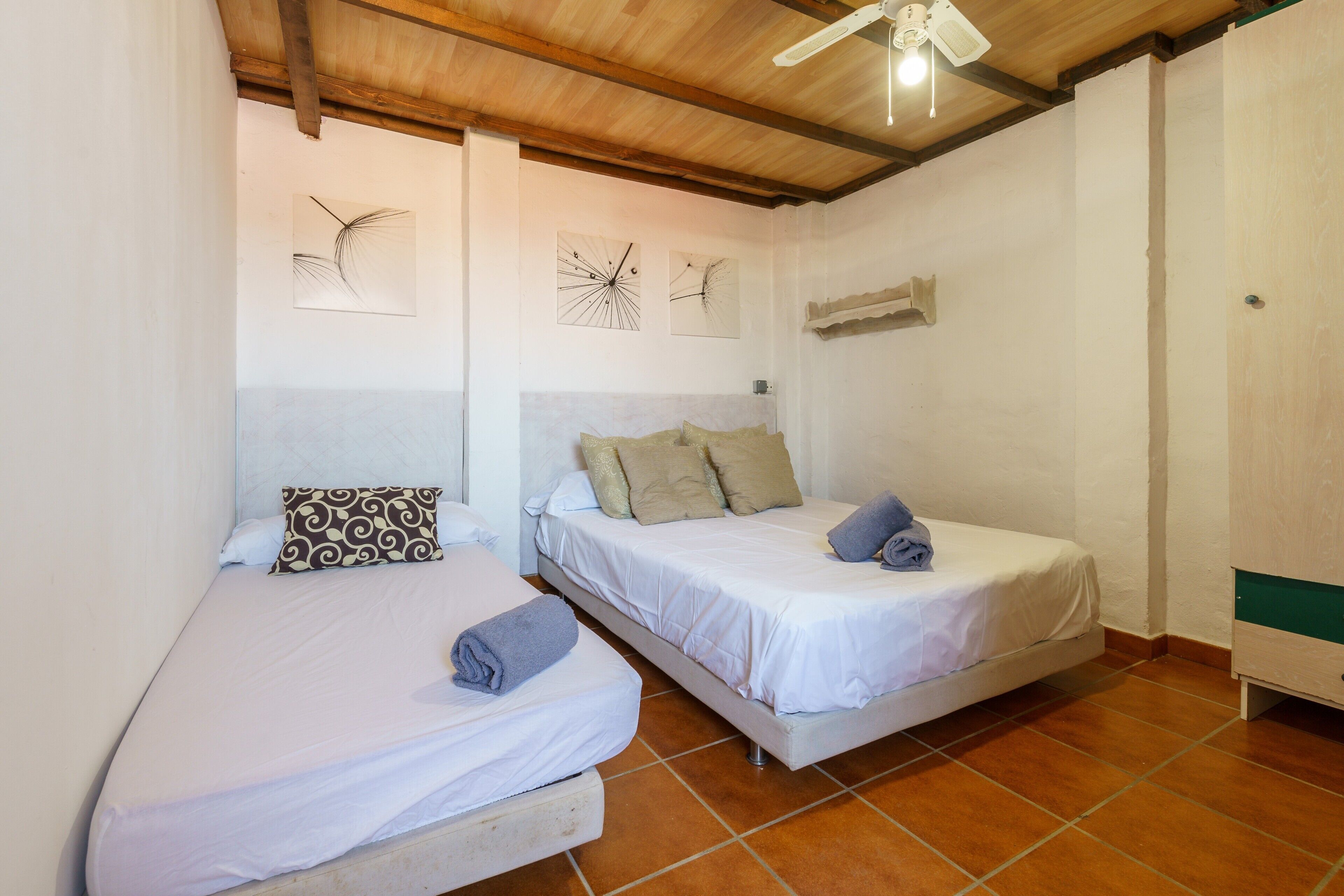 A room with two single beds, a ceiling fan, and a wall clock.