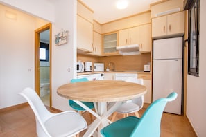 Une cuisine compacte avec une table ronde en bois, des chaises blanches et un réfrigérateur blanc.