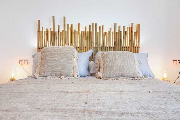 Un lit avec une couverture à motifs, deux oreillers, une tête de lit en bambou et des lampes de chevet.