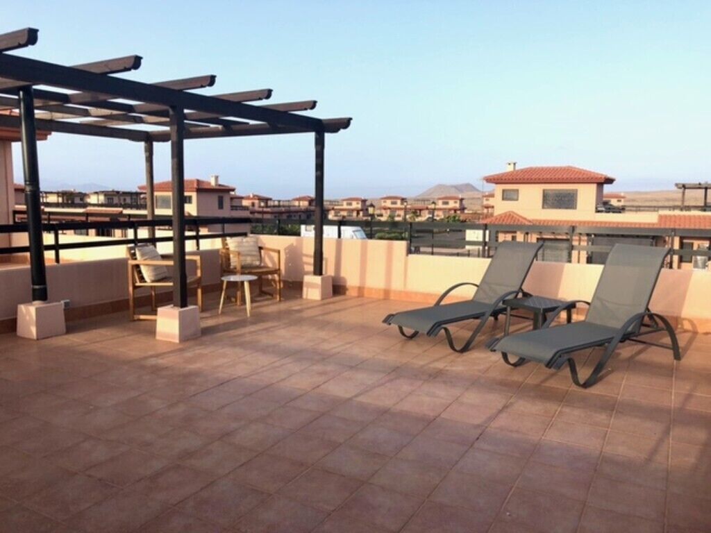 A rooftop terrace with lounge chairs, a pergola, and a view of buildings in the distance.