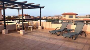 A rooftop terrace with lounge chairs, a pergola, and a view of buildings in the distance.