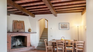A room with a fireplace, wooden dining table, chairs, a staircase, and a framed picture on the wall.