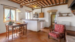 A spacious kitchen with wooden beams, a dining area with a red upholstered chair, and a central island with a sink and cabinets. - Universal Harmony - Usignolo Agriturismo with Mountain View and Shared Pool (Dicomano)