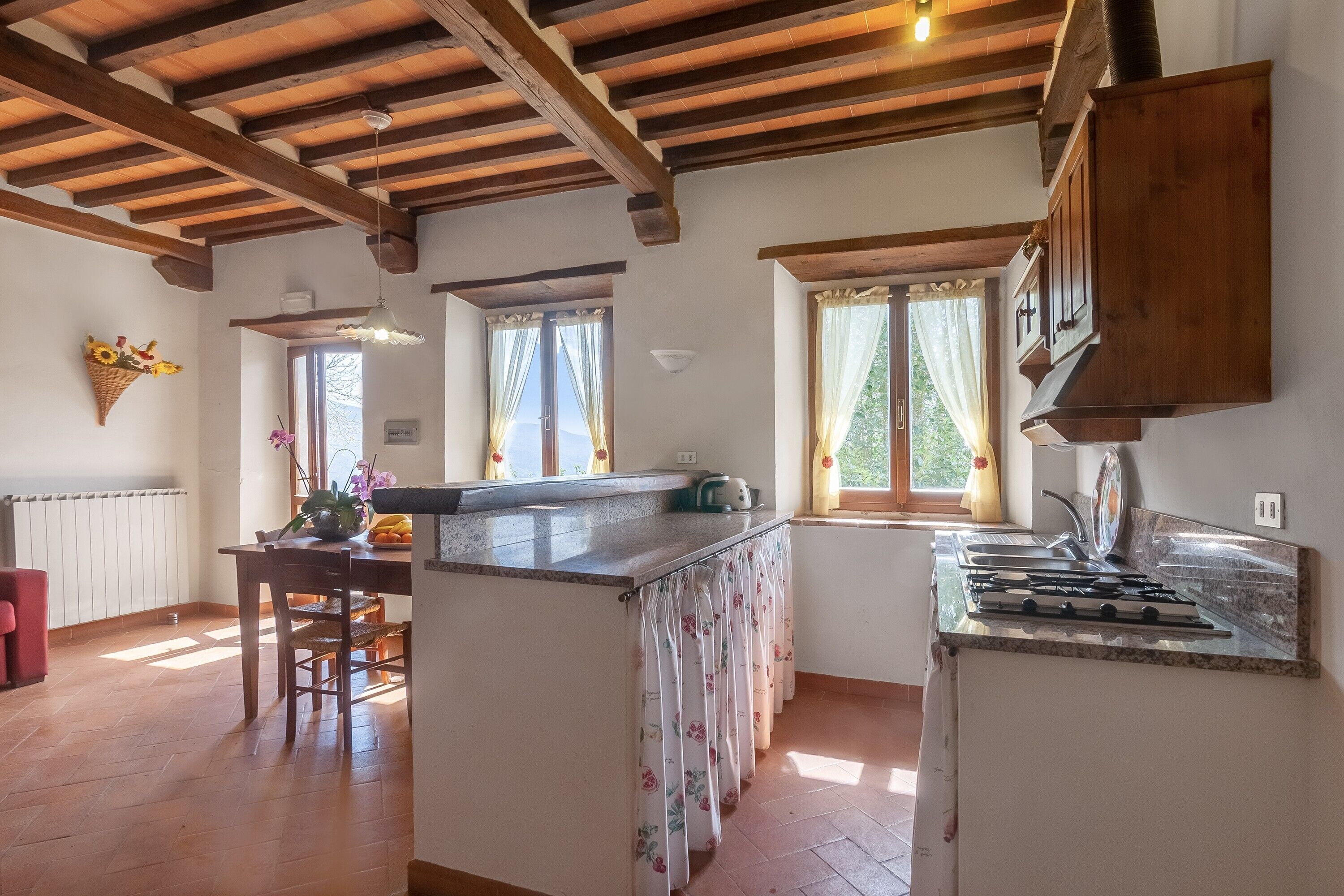 A kitchen with wooden beams, a gas stove, a sink, and a window with curtains.