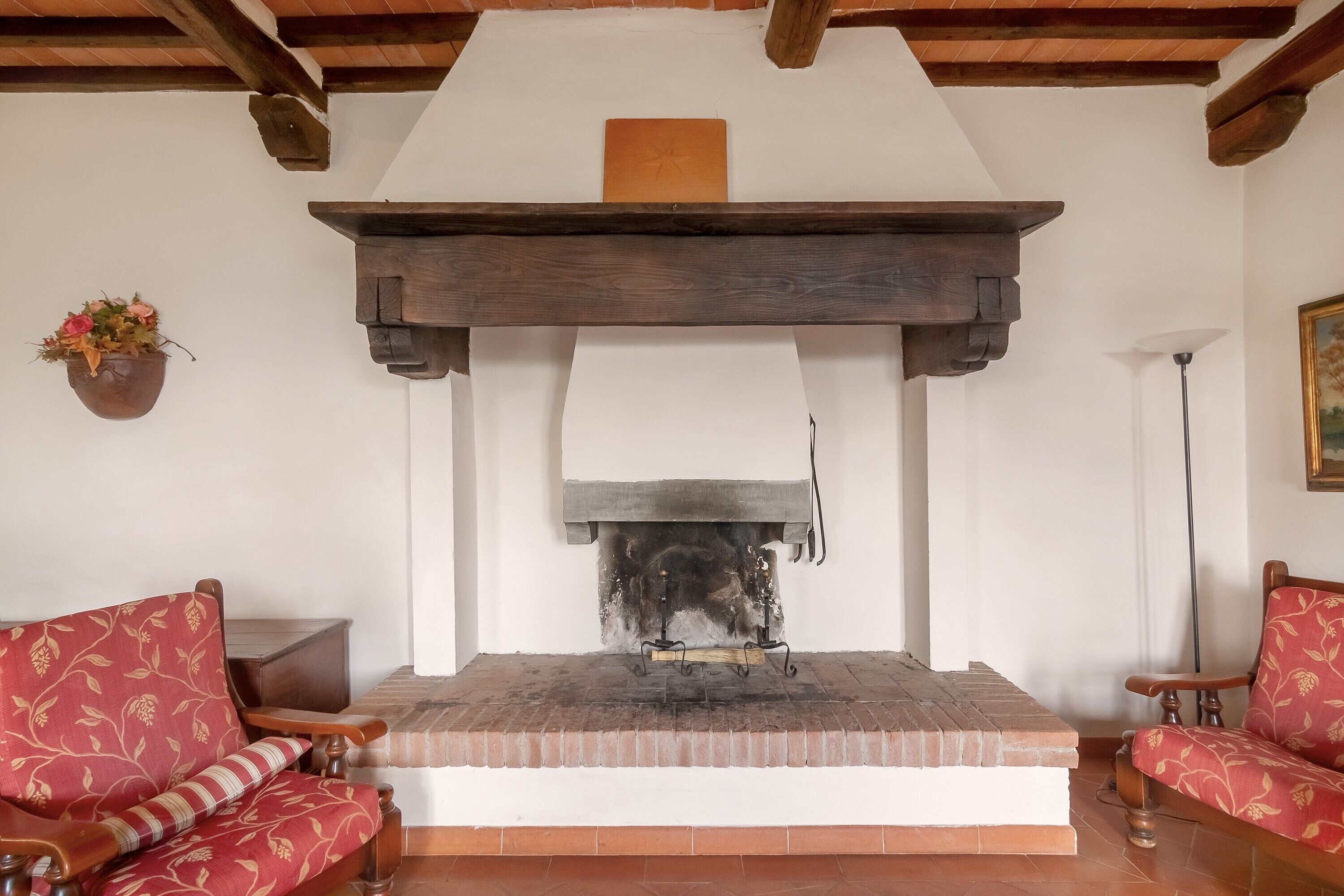 Une cheminée avec un manteau de cheminée, deux fauteuils rouges recouverts de tissu et un banc en bois.
