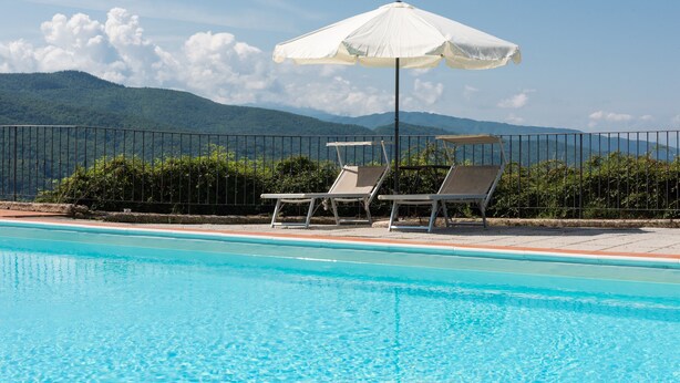 A swimming pool with lounge chairs and an umbrella, surrounded by a fence and greenery, with mountains in the background. - Universal Harmony - Usignolo Agriturismo with Mountain View and Shared Pool (Dicomano)