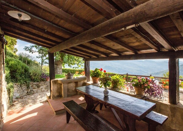 Un espace extérieur abrité, doté d’une table et de bancs en bois, entouré de plantes en pot et offrant une vue panoramique sur les montagnes.
