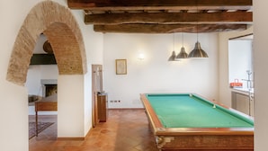 Une table de billard dans une pièce dotée d’une arche en briques rustiques, de poutres en bois et de luminaires suspendus.