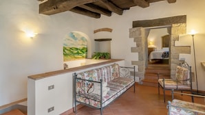 A rustic interior with a wooden ceiling, a sofa with floral upholstery, a bench, and a staircase leading to another room.