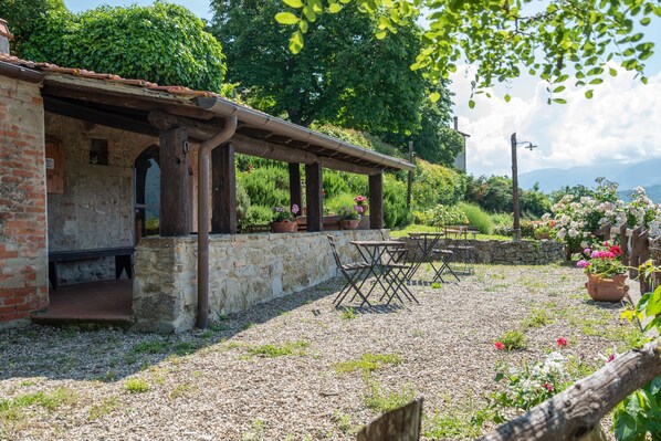 Une terrasse extérieure rustique, agrémentée d’un mur en pierre, d’une pergola en bois et d’un sol en gravier.