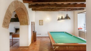 Una mesa de billar con superficie de fieltro verde, vigas de madera y un arco de ladrillo rústico.