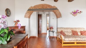 Una habitación con una mesa de comedor de madera, un sofá, un arco de ladrillo y un arreglo floral colgado en la pared.