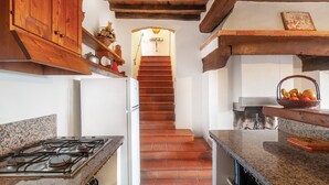 Una cocina con estufa a gas, armarios de madera, una escalera que sube a un altillo y un techo rústico.