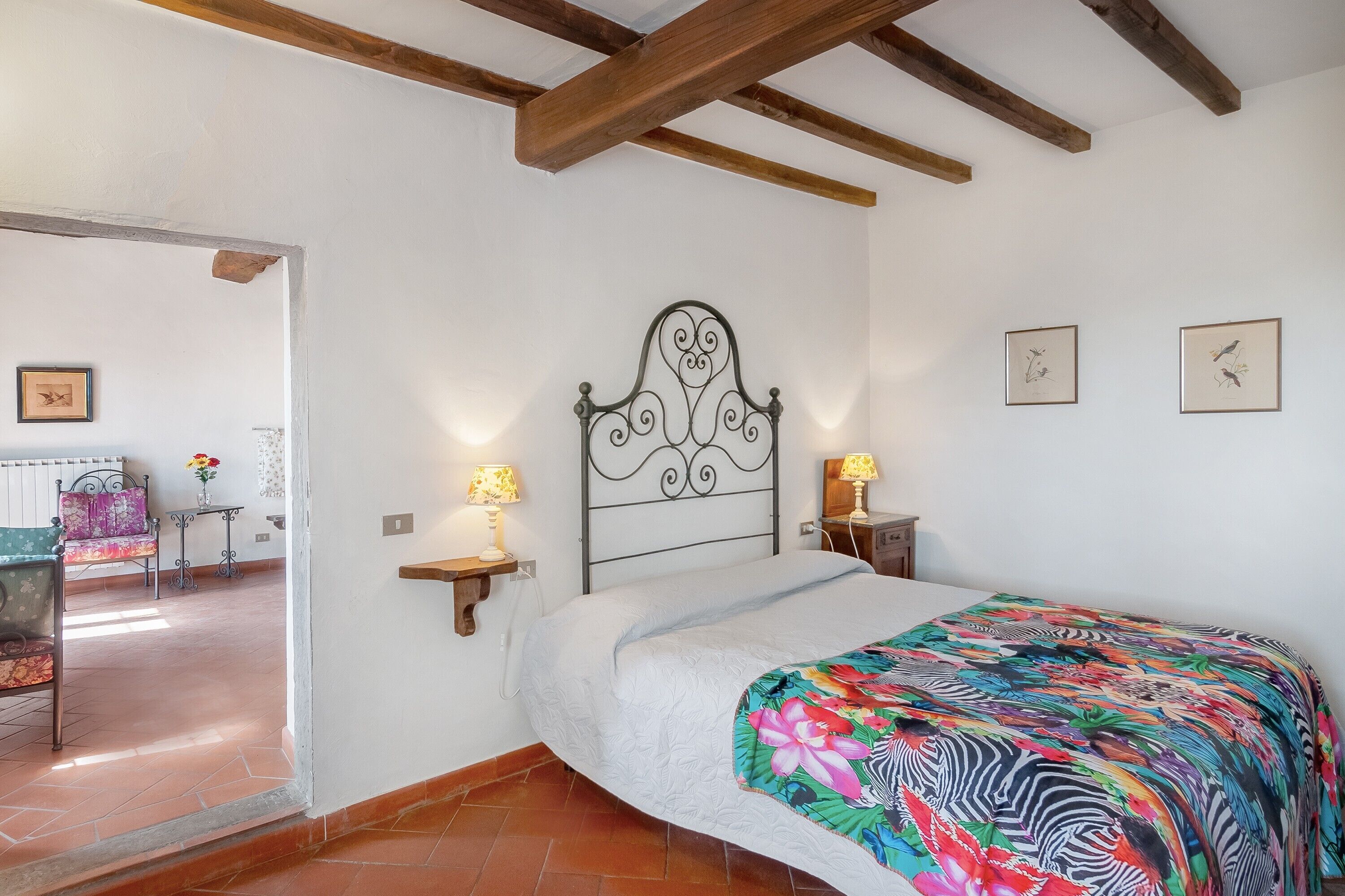 Un dormitorio con cama, mesita de noche, lámpara de pared, cabecera de madera y vistas a otra habitación.