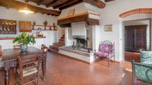 Un interior rústico con una mesa de comedor de madera, sillas, una chimenea y una escalera que sube a un nivel superior.