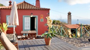 Un bâtiment rouge avec un toit en tuiles, une table sur laquelle est posée une plante en pot et une chaise.