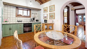 Une cuisine avec des meubles de rangement verts, un coin repas avec des chaises en osier et une table ronde en verre.