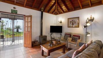 Una sala de estar con techo de madera, televisor, muebles de mimbre, chimenea y un cartel que indica una salida.