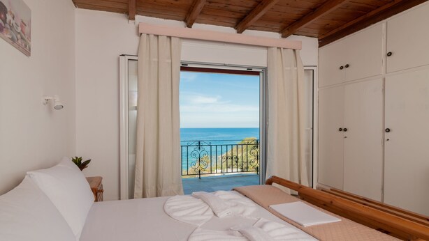 A bedroom with a bed, a wardrobe, a balcony with a view of the sea, and a painting on the wall. - Agnadi Sea View Apartments (Zakynthos)