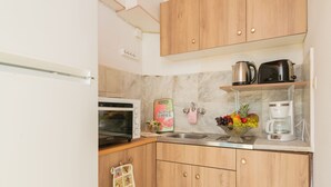 A compact kitchen with wooden cabinets, a microwave, a coffee maker, and a fruit bowl. - Agnadi Sea View Apartments (Zakynthos)