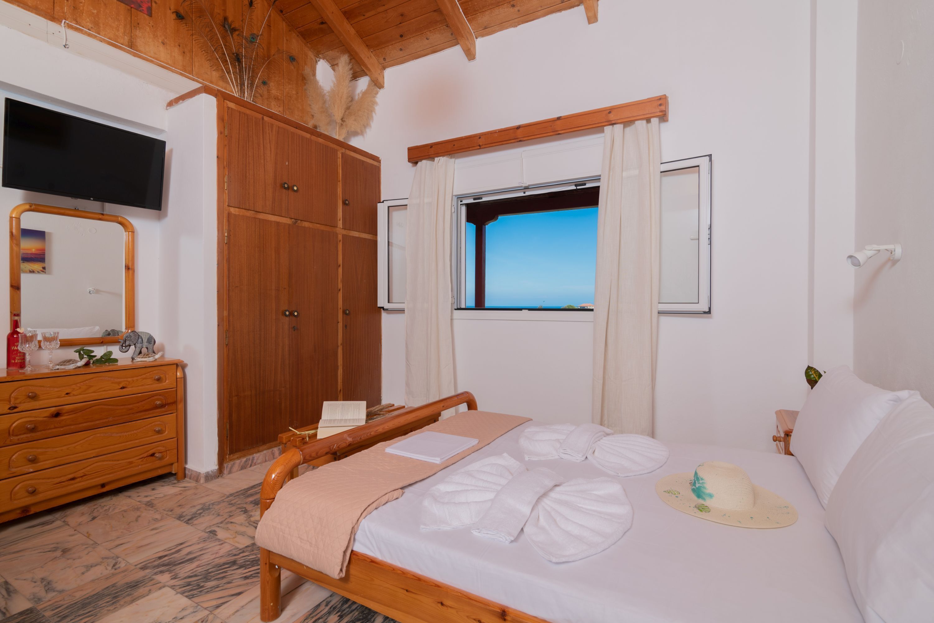 A bedroom with a wooden bed, a dresser, a television mounted on the wall, and a window with curtains.
