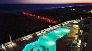 Ein Schwimmbecken mit spiralförmigem Design, umgeben von Liegestühlen und Blick auf den Ozean im Sonnenuntergang.