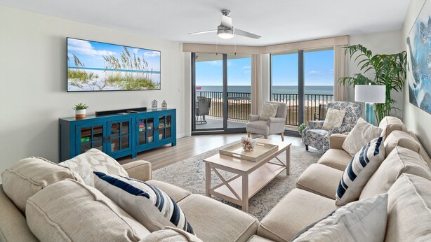 Ein geräumiges Wohnzimmer mit einer großen Couch, einem Couchtisch und einem Fernseher. Ein Balkon bietet Blick auf das Meer.