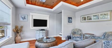 Una sala de estar con ventilador de techo, televisor de pantalla plana, sofá, una silla y una mesita.