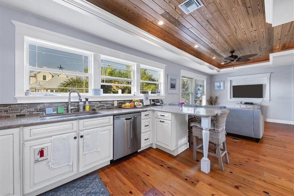 A modern kitchen with white cabinets, a built-in dishwasher, and a dining area with a gray sofa and wicker chairs.