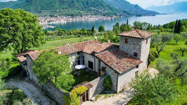A stone villa with a tiled roof, surrounded by lush greenery and a view of a lake and mountains. - Casale Lucrezia - Salò (Salò)