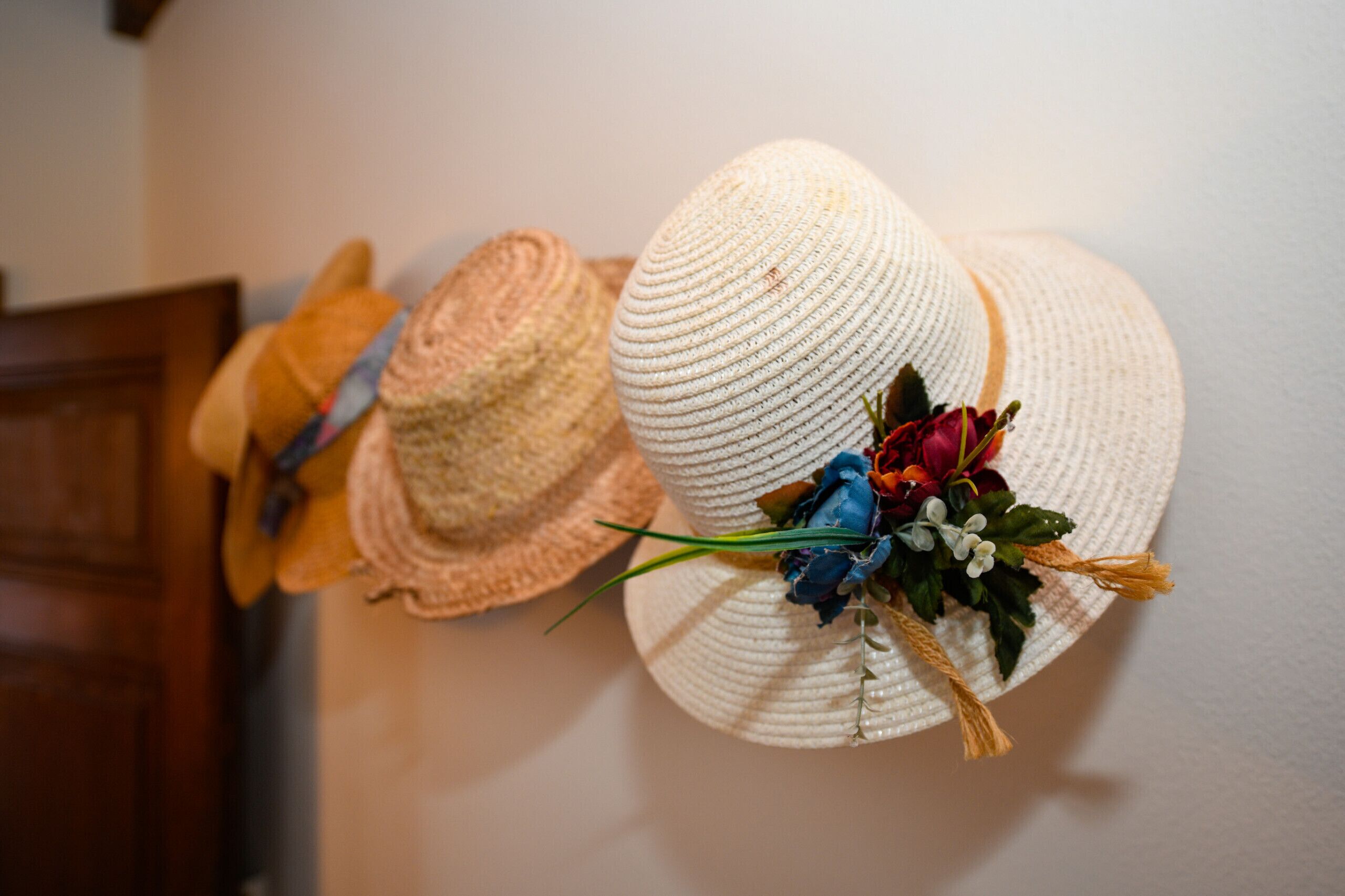 A wall with three straw hats, one with a floral decoration.