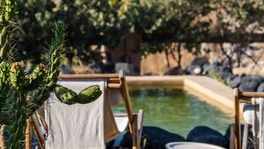 A pool area with a wooden chair and a towel, surrounded by cacti and rocks. - Aurora Villa by K&K (Santorini)
