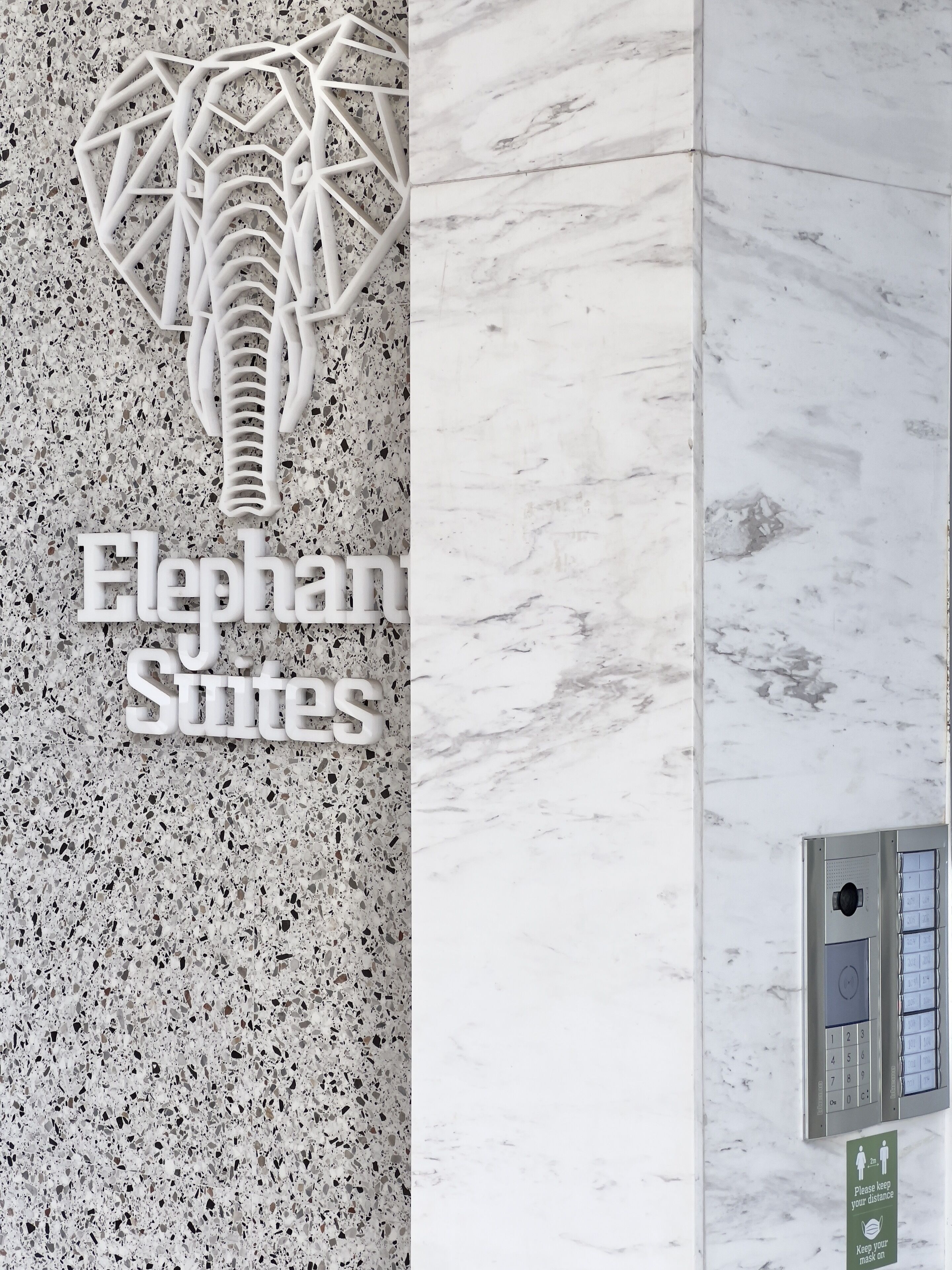 A sign for 'Elephant Suites' with a unique elephant sculpture design, a marble wall, and a keypad entry system.