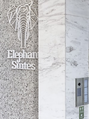 A sign for 'Elephant Suites' with a unique elephant sculpture design, a marble wall, and a keypad entry system. - Elephant Suites (Thessaloniki)